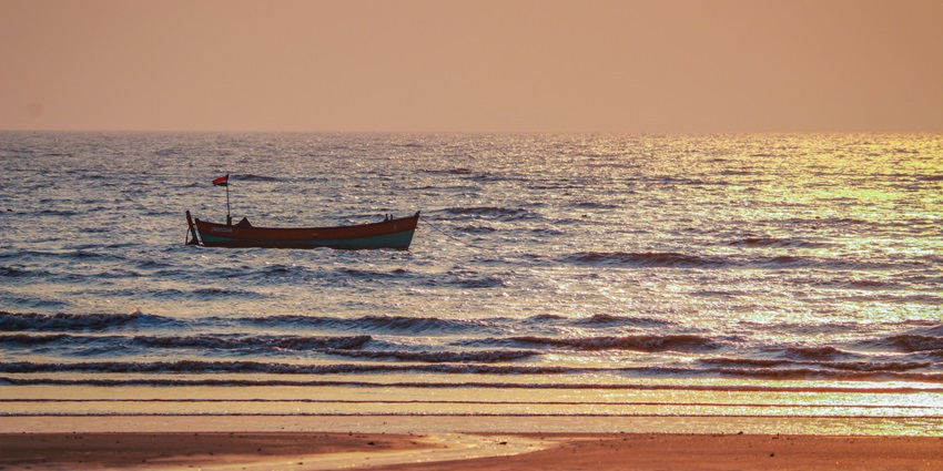 A scenic view of sunset at the Tithal Beach with a boat floating on the vast ocean.