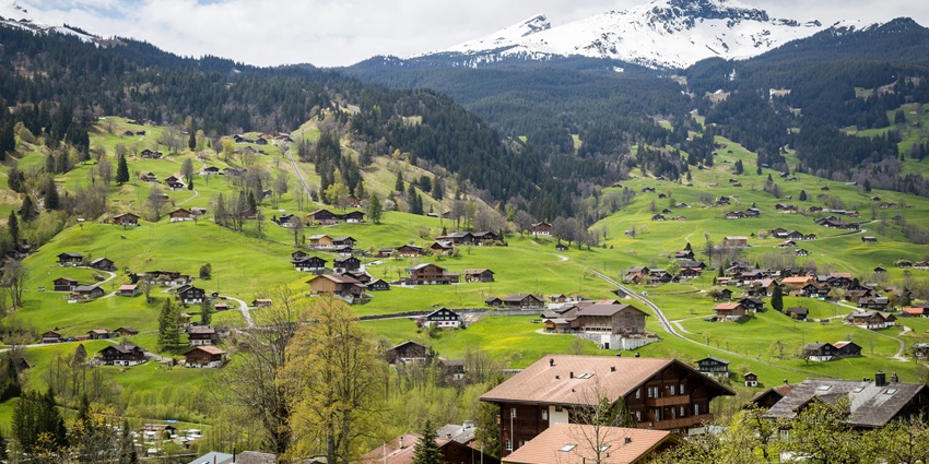 Panoramic view of a town surrounded by the lush green hills and snow-capped mountain