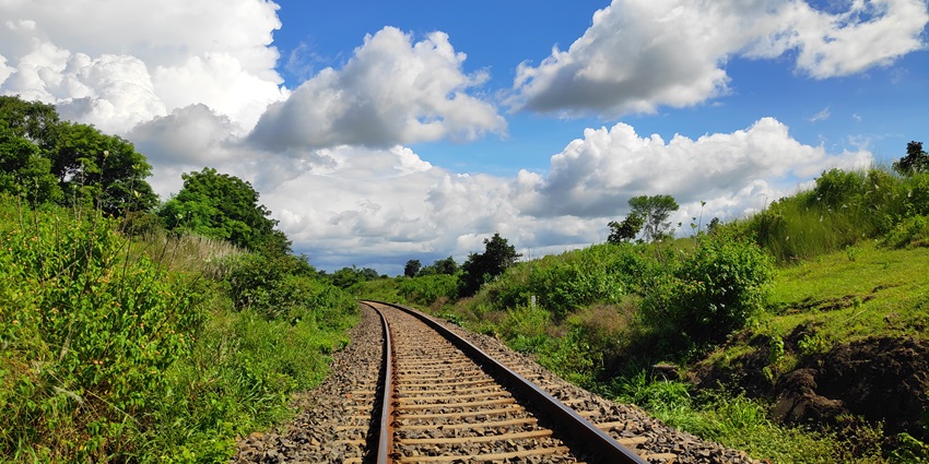 View of a rail track with lush green vegetation and cloudy skies in the background