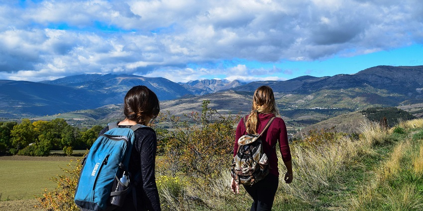 Picturesque view of mountain trails surrounded by lush greenery and two girls trekking.