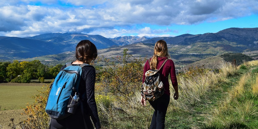 Two women trekking along a rugged trail, surrounded by scenic natural landscapes.