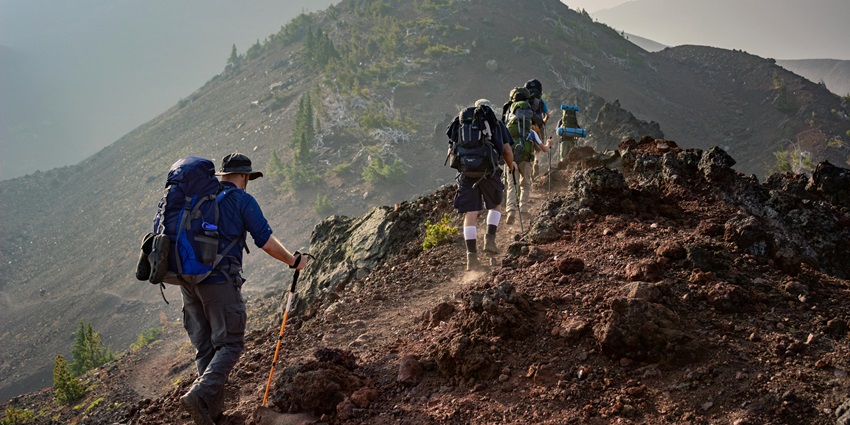 Group of hikers trekking through rugged mountain terrain, surrounded by towering peaks.