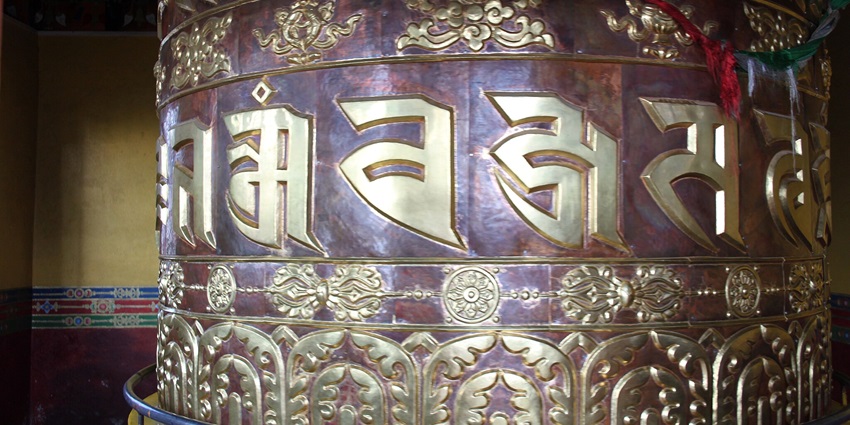 A picture of a prayer wheel in a Buddha temple with Buddhist texts carved on the wheel itself