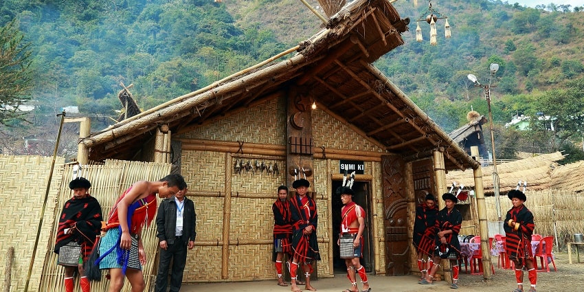 A stunning view of a lot of people standing in front of a bamboo hut in a village.