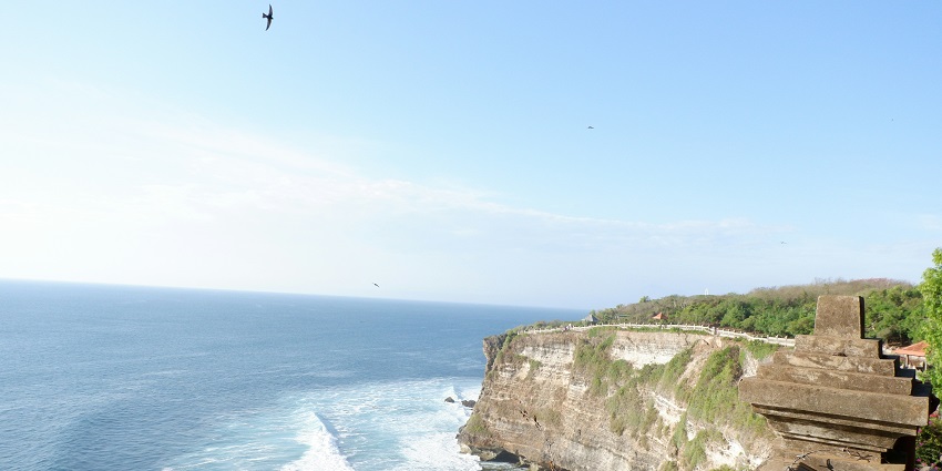 A breathtaking view of a body of azure waters from a temple on a big rocky cliff.