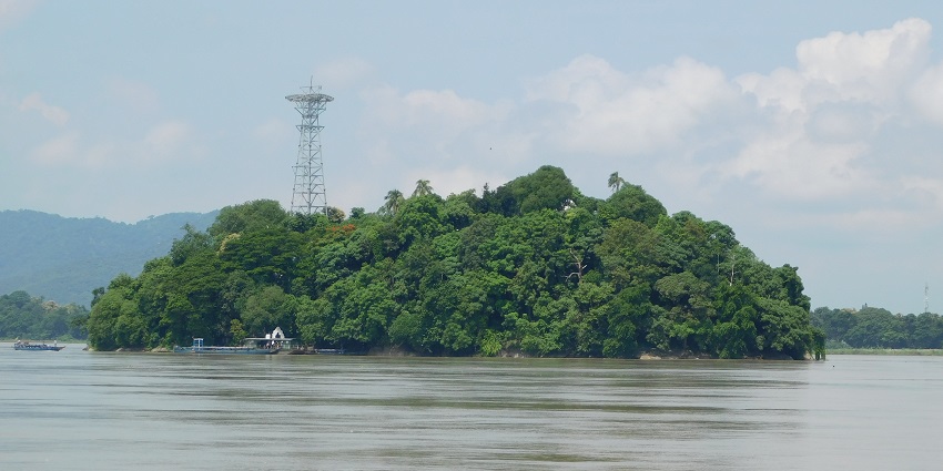 :A captivating view of Umananda Island with lush greenery & backdrop of cloudy sky.