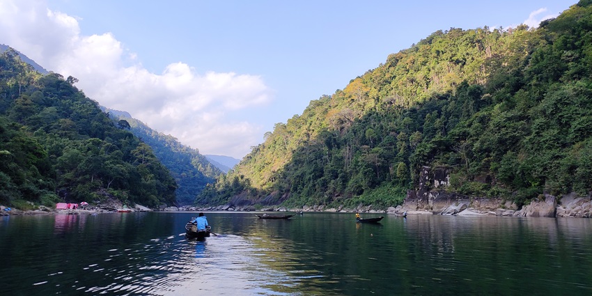 Crystal-clear Umngot River with boats floating on turquoise water, surrounded by green hills.