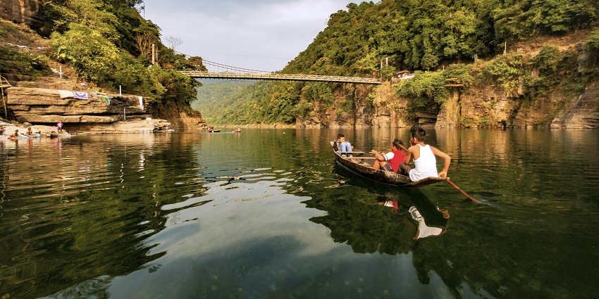 Dawki Bridge spanning the clear, blue Umngot River with lush green hills in the background.