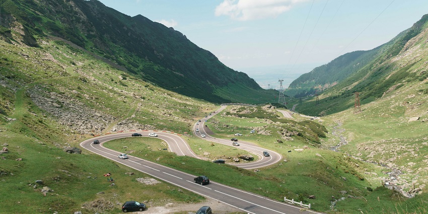Scenic view of cars driving on a road surrounded by mountains under a clear blue sky.