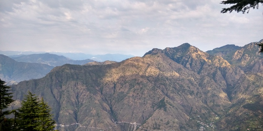 Panoramic landscape from above, featuring rolling hills and a bright, sunny sky.