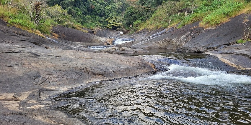 View of Kozhippara Waterfalls with cascading water surrounded by dense, green forest.