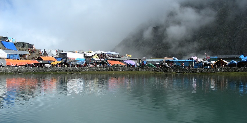 Serene view of Manimahesh Lake surrounded by majestic mountains and clear blue skies.