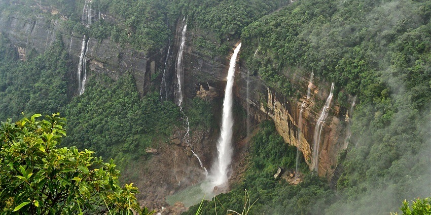 View of Nohkalikai Falls plunging into a lush, verdant valley with misty surroundings.