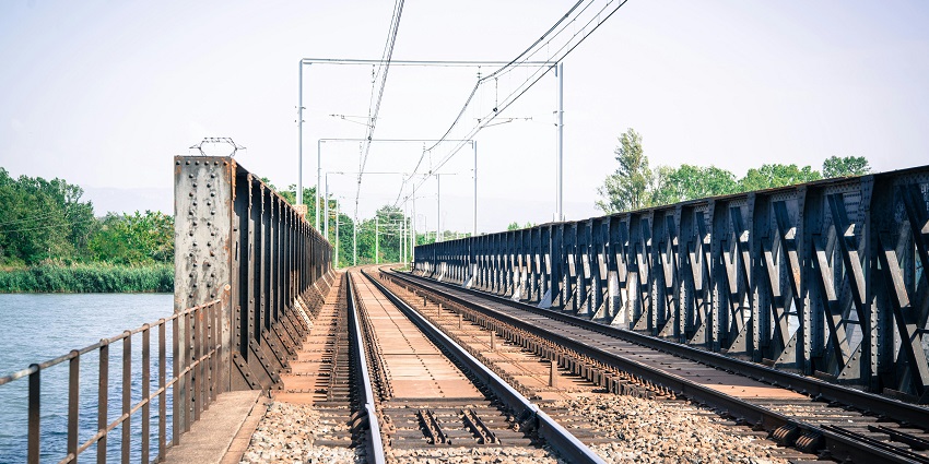 Image of railway tracks over a bridge and water. Surrounded by lush greenery.