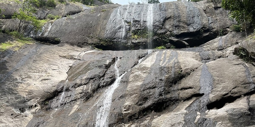 Thusharagiri Waterfalls cascading down rocky terrain, surrounded by lush greenery.