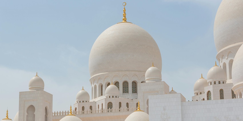 Image of a grand Mosque designed beautifully with white marvels and gold on top.