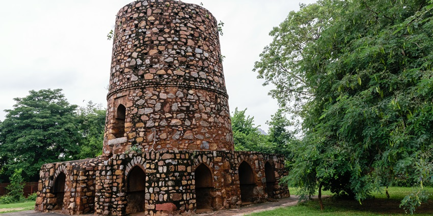 A frontal view of a historical minaret with a lush garden area all around