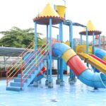 View of a blue, yellow and red water slide and a pool in a water park during the daytime.