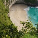 A breathtaking aerial view of a turquoise water body near a green cliff during the day.