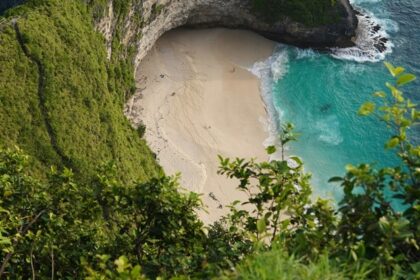 A breathtaking aerial view of a turquoise water body near a green cliff during the day.