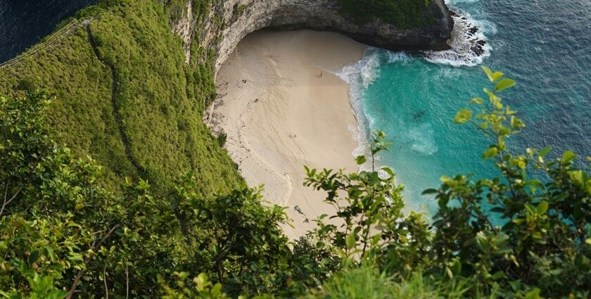 A breathtaking aerial view of a turquoise water body near a green cliff during the day.