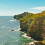 A breathtaking view of a turquoise water body near a lush green cliff during the daytime.