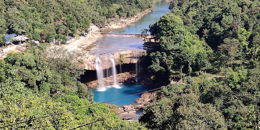 Krang Suri Waterfall cascading over rocky terrain surrounded by lush green vegetation.