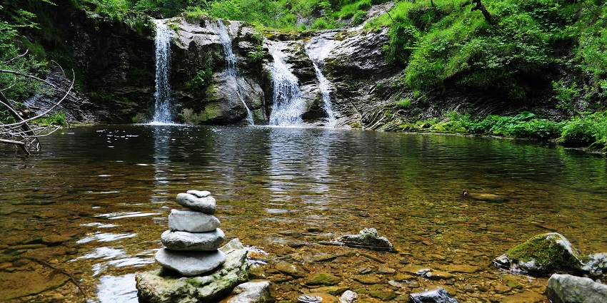 Waterfall in the forest with water cascading down rocky terrain, surrounded by dense greenery.