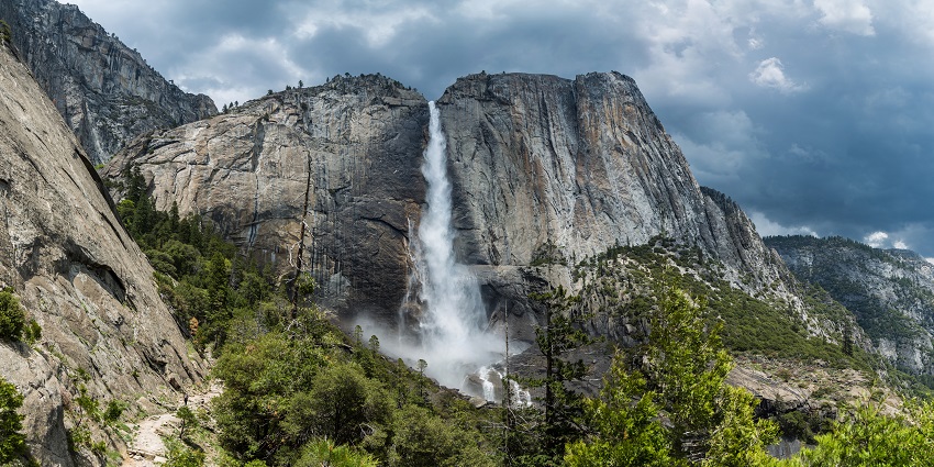 A scenic view of a waterfall cascading down the rocky mountains with lush green trees.