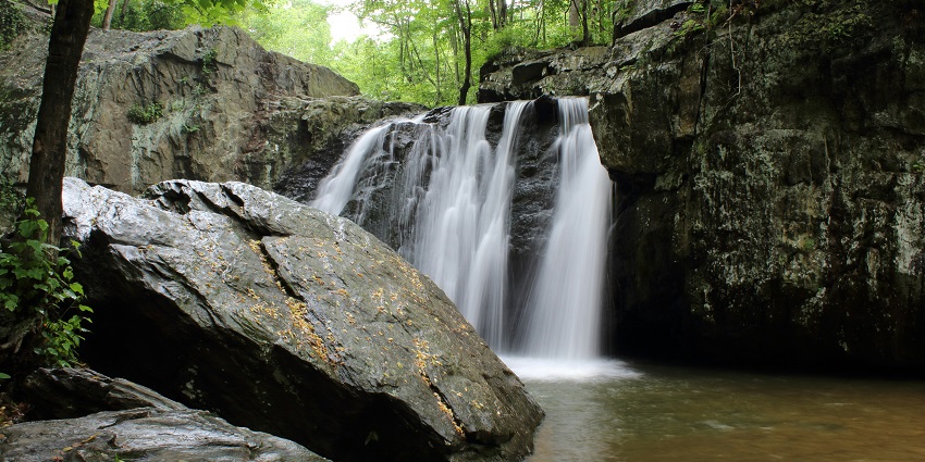 Stunning waterfall cascades down rocky cliffs, surrounded by lush greenery and vibrant nature.