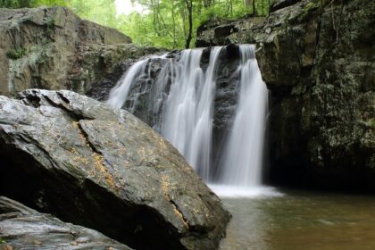 A stunning vista of water pouring down from rocky cliffs and merging the tranquil river.