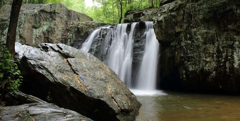 A stunning vista of water pouring down from rocky cliffs and merging the tranquil river.