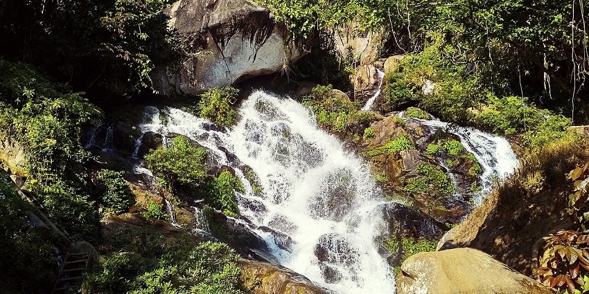 Waterfall in Manjha cascading down rocky cliffs, surrounded by lush greenery and beauty.