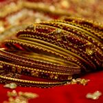 A picture of the bangles of a bride placed on a red cloth with embroidery in a slanting position