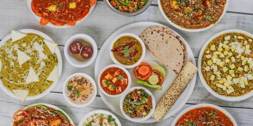 An image of multiple food items of delectable Indian cuisine served on a white table.