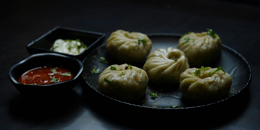 A picture of momos served with a red dip on a black plate at a restaurant