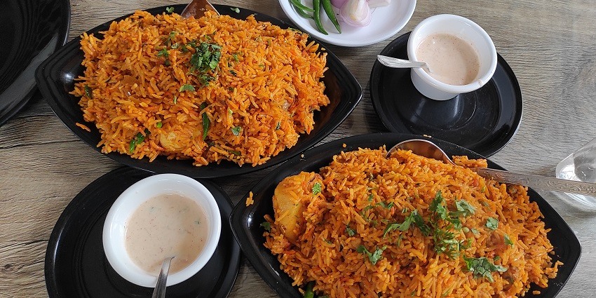 A picture of a rice dish served on a restaurant table along with dips and raw onions, all in black cutlery