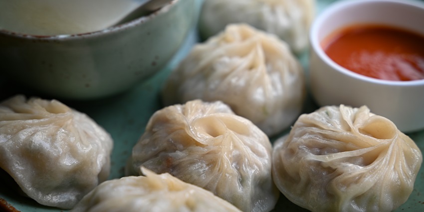 A plate of steamed momos served with red chilli sauce
