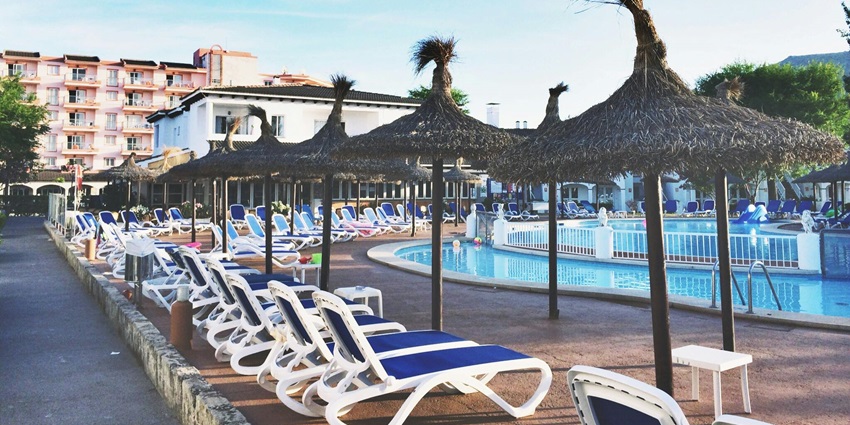 A picture of a resort with shade umbrellas and beach chairs placed around a swimming pool