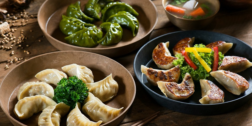 A mouth-watering view of three plates of different cloured dumplings served with a dip.