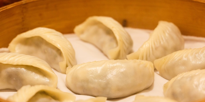 A mouth-watering view of a plate of momos in a brown box during the daytime for all.