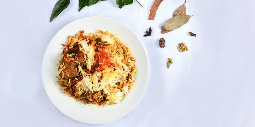 A mouth-watering view of a white plate served with biryani with spices on the side.
