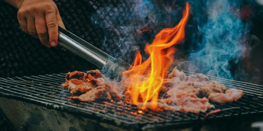 A delicious view of a man cooking food on a grill during the daytime, which all can enjoy.