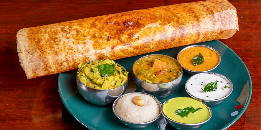 A mouth-watering view of a plate with dosa and bowls with different cooked vegetables.