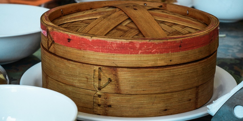 A tempting view of a container kept on a table with dumplings in it with plates beside it.