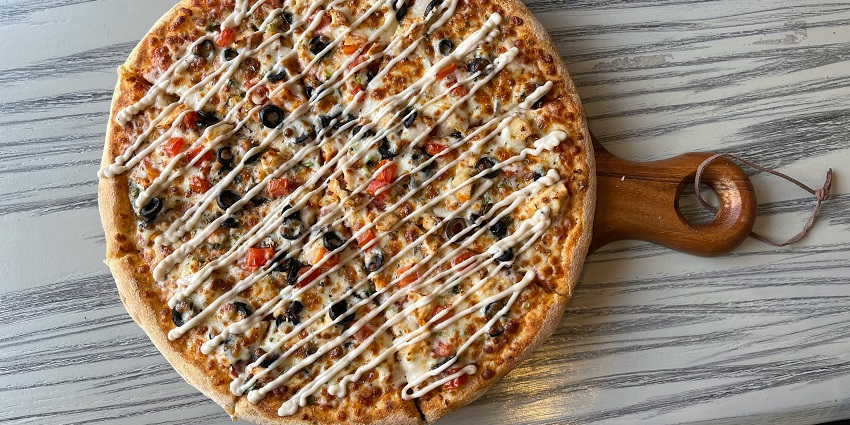 A tempting view of a round pizza with a lot of toppings served on a brown table.
