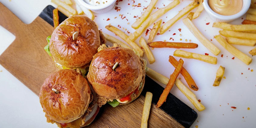 A mouth-watering view of a plate on a table with hamburgers, fries and a dip on the side.