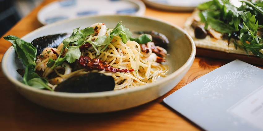 A tempting view of a ceramic plate served with pasta garnished with green vegetables.