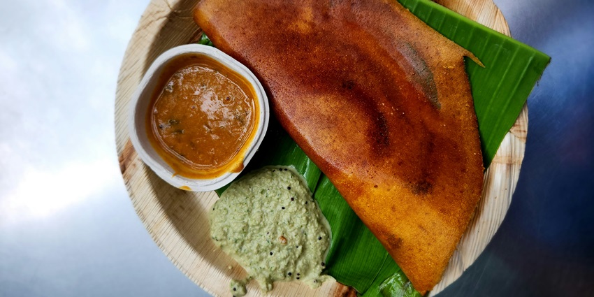 A mouth-watering view of a brown plate served with dosa and sambar on a leaf on a table.
