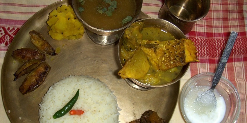 A mouth-watering view of a plate served with different dishes, rice, curd and a glass.